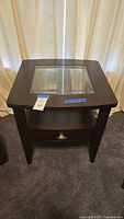 Front view of the dark brown wood side table with glass top, lower shelf, and drawer closed.