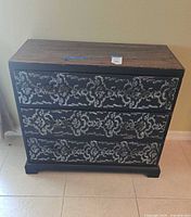 Front view of decorative chest showing three drawers with distressed finish and intricate white pattern.