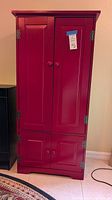 Front view of the red wooden cabinet showing the full height with upper and lower hinged paneled doors.