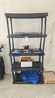 Full view of black plastic shelving unit with items on shelves and floor