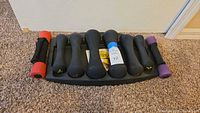 Eight hand weights in various sizes (1, 3, 5, 8 lbs) arranged on a black dumbbell rack, showing all weights from top view. Two 1 lb weights have red and purple colored ends.