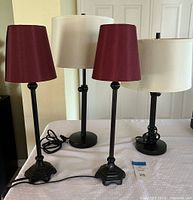 Two red lamps with tapered red fabric shades and ornate black metal bases displayed on a white table.