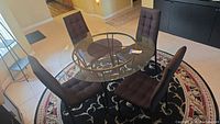 Overhead angled view of round glass top table and 4 brown upholstered chairs on patterned rug.