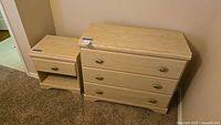 Photo showing both the small dresser and matching nightstand side by side on carpeted floor against a wall.