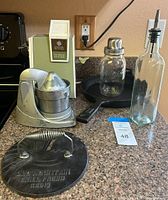 General view of vintage General Electric can opener and ice crusher with other items including Streamline Super-Juicer, cast iron skillet, Old Mountain grill press, mason jar shaker, and olive oil bottle