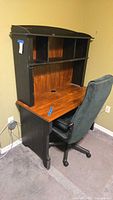 Front view of wood computer desk with hutch and swivel office chair; desk has a distressed black frame with brown wood surface and multiple shelves in hutch section