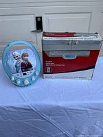 Frozen karaoke CD player and boxed GPX under-cabinet CD radio on table