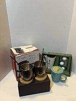 Group shot of all items: coffee maker box, mule mugs on coasters, Dad golf mug set, teal MOM mug