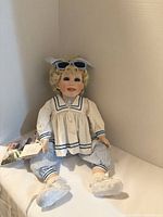 Full view of porcelain doll seated showing outfit and accessories