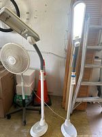 Two white OttLite floor lamps standing upright, one lamp has a flexible neck and rectangular light panel, cord plugged in and one lamp is missing bulbs.