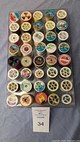 Top view of approximately 40 sewing thread spools, arranged in a clear plastic storage tray with a lid underneath