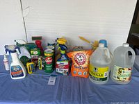 Multiple household cleaning products including vinegar jugs, baking soda, Comet cleanser, and several spray bottles arranged on a blue tablecloth.