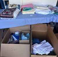 Photo showing assortment of folded fabric on table and fabric pieces in boxes beneath