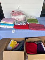 Wide view of fabric assortment on table and in boxes showing multiple folded fabrics in different colors and patterns