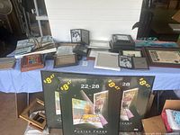 Large assortment of picture frames and canvas art on table, showing various sizes and styles including colorful and neutral frames and paintings.