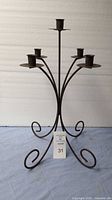 Black wrought iron candle stand with five arms for holding candles, four metal holders visible on stand