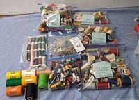 Wide view showing assorted spools and bobbins of threads in various colors and types with some items bagged and labeled for sorting.