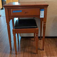Wooden sewing cabinet with drawer, closed top, and black padded bench set beneath