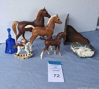 Photo showing seven decorative items including three horse figurines of different sizes, small rocking horse with rider, cobalt blue glass bell, quartz geode, and small wooden display shelf.