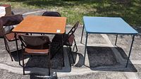 Both folding card tables, brown and gray with visible wear, set outside on paved area