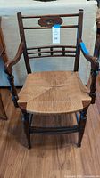 Front view of vintage wooden chair with woven rush seat, armrests and decorative backrest.