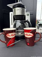 Front view of Black & Decker coffee maker with glass carafe and two Tim Hortons mugs