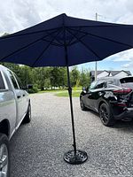 Full view of blue patio umbrella set up between vehicles, showing cast-iron base