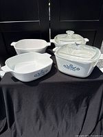 Four white CorningWare casseroles and two glass lids displayed on table