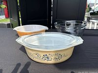 Three glass kitchen pieces: Pyrex Homestead casserole with lid front, Fire King peach lustre casserole back left, Anchor Hocking clear bowl back right