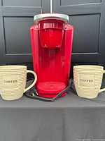Front view of red Keurig brewer with two beige mugs