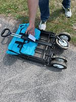 Folded state of the beach wagon showing the handle, metal frame, fabric, and wheels.