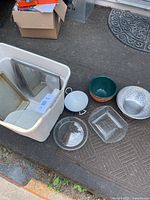 Overview of assorted kitchen items including bowls, glass baking dishes, and colander placed on a textured floor surface.