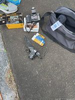 Photo showing two cameras, one Kodak Medalist VR35 with original box, two travel bags, and film rolls on outdoor surface.