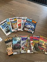 Overview photo of 13 mixed automotive magazines laid out on a wood floor showing a variety of titles and cover images featuring cars and automotive themes.