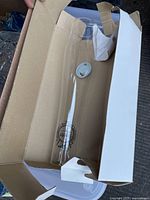 Glass chimney visible inside a brown cardboard box with a white outer cover.