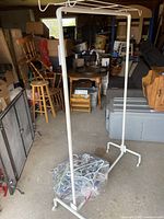 White metal portable clothes rack standing on concrete floor with furniture in the background.