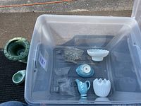 Clear plastic bin containing clear crystal candle holders, small blue ceramic pitcher and bowl, white milk glass items.