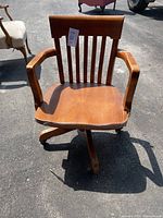 Front view of vintage wood desk chair showing curved backrest with vertical slats, armrests, contoured seat, and castered base.