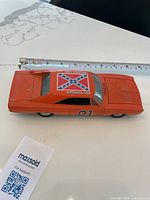 Top view of the General Lee die cast model car on a white surface measuring approximately 8 inches in length. Features include the orange body, Confederate flag decal roof, and '01' side marking.