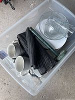 Plastic container holding assorted glass and ceramic dishes including clear glass bowls, white ceramic bowls, green marble pestle and mortar, and a folded dark pinstripe cloth item.
