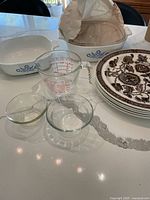 Image of Pyrex measuring cup, clear glass bowls, CorningWare white baking dishes with blue cornflower pattern, and Jacobean ironstone plates with brown floral pattern