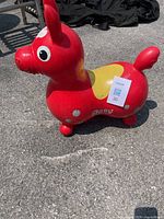 Side view of red inflatable Rody bounce toy donkey on pavement, visible wear, needing air.