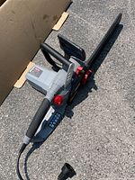 Full view of Oregon electric chainsaw placed on asphalt surface showing body, handle, and bar with chain guard.