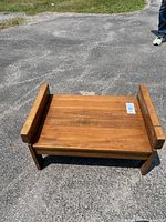 Top view of solid wood foot stool/bench on asphalt showing rectangular shape and raised side supports.