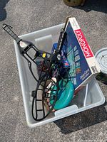 Plastic bin containing Monopoly board game, Katamino puzzle pieces, Jumbling Towers blocks, and white chalk sticks.