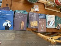 Overhead view of a collection of Great Courses books and DVD cases displayed on a wooden chair, covering various subjects like physics, literature, and philosophy.