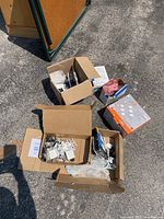 Boxed hardware items including assorted door hinges, electrical switches and switch covers, and a red hard hat helmet in packaging.