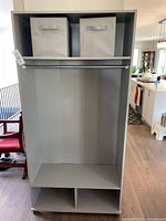 Front view of the grey IKEA shelving unit with two fabric baskets on top shelf, metal hanging rod below, and lower cubbies.