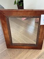 Full view of square mirror with warm wood frame and carved geometric border showing the overall size and design.