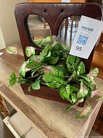 Front view of walnut wood frame with butterfly-shaped mirror cutout and attached planter holding green foliage.